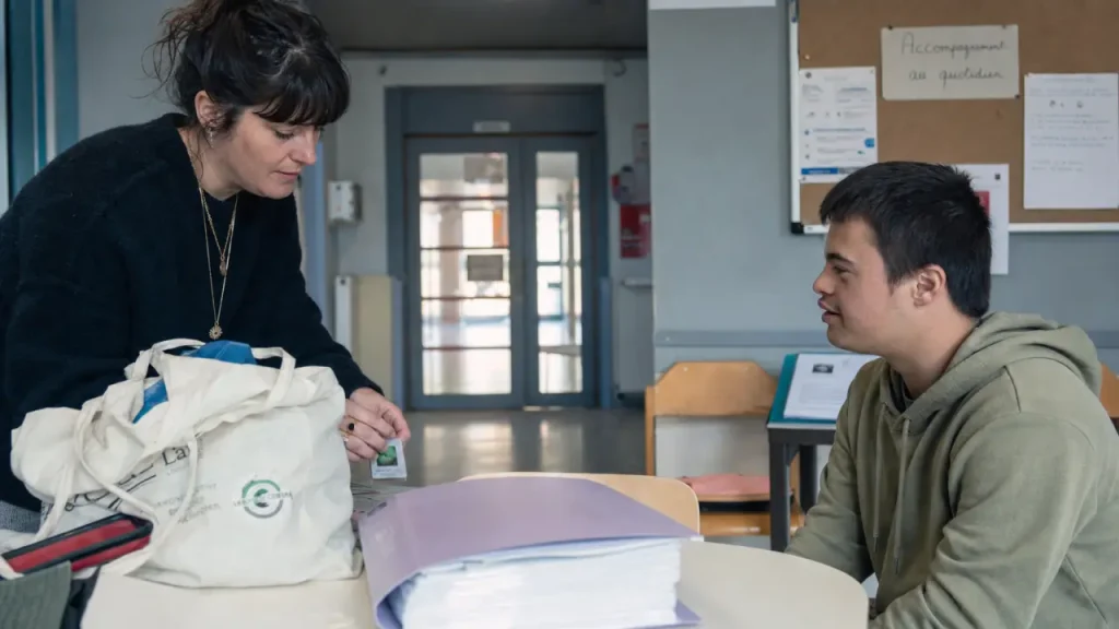 Travailler avec des handicapés : éducatrice ajuste un matériel, élève observe en établissement médico-social